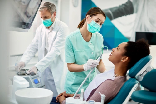 dental assistant rinsing patient mouth during cleaning with dentist in background